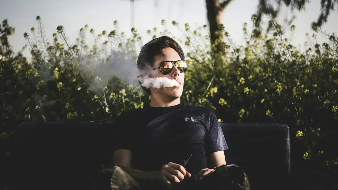 Man vaping on a bench in a park.